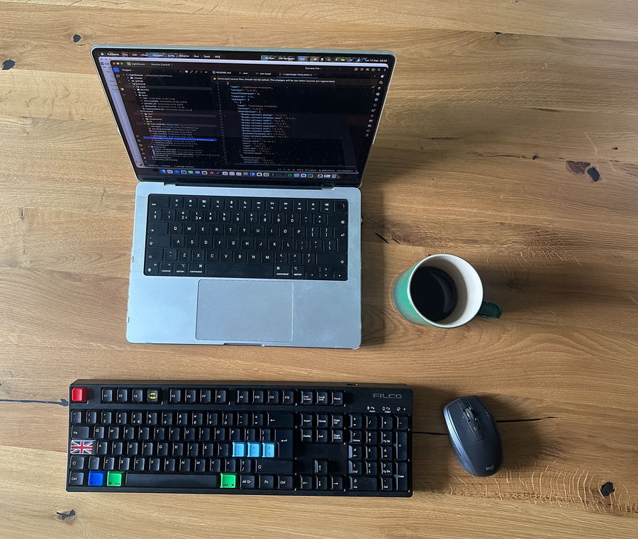 macbook on a oak table together with a mechanical keyboard and a coffee